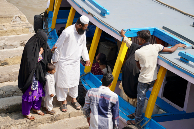 Muslim family boarding boat; the woman wears a chador.